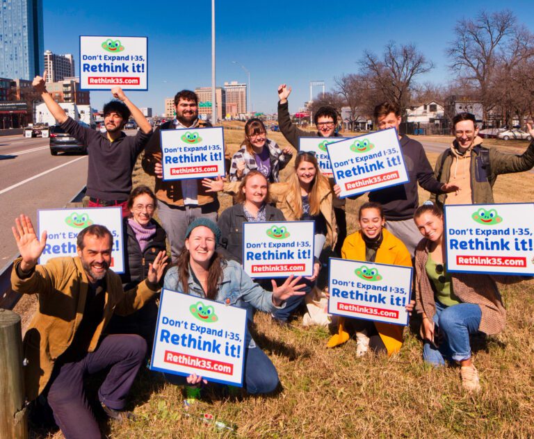 A group of smiling transportation advocates beside I-35 holding signs, Don't expand I-35. Rethink it!